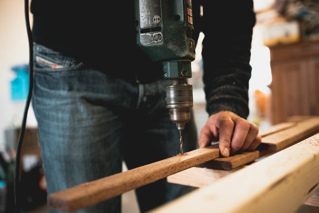 Cristian Flore Aranjuez - Close-up of a person using an electric drill on a wooden plank, showcasing detailed woodworking skills.