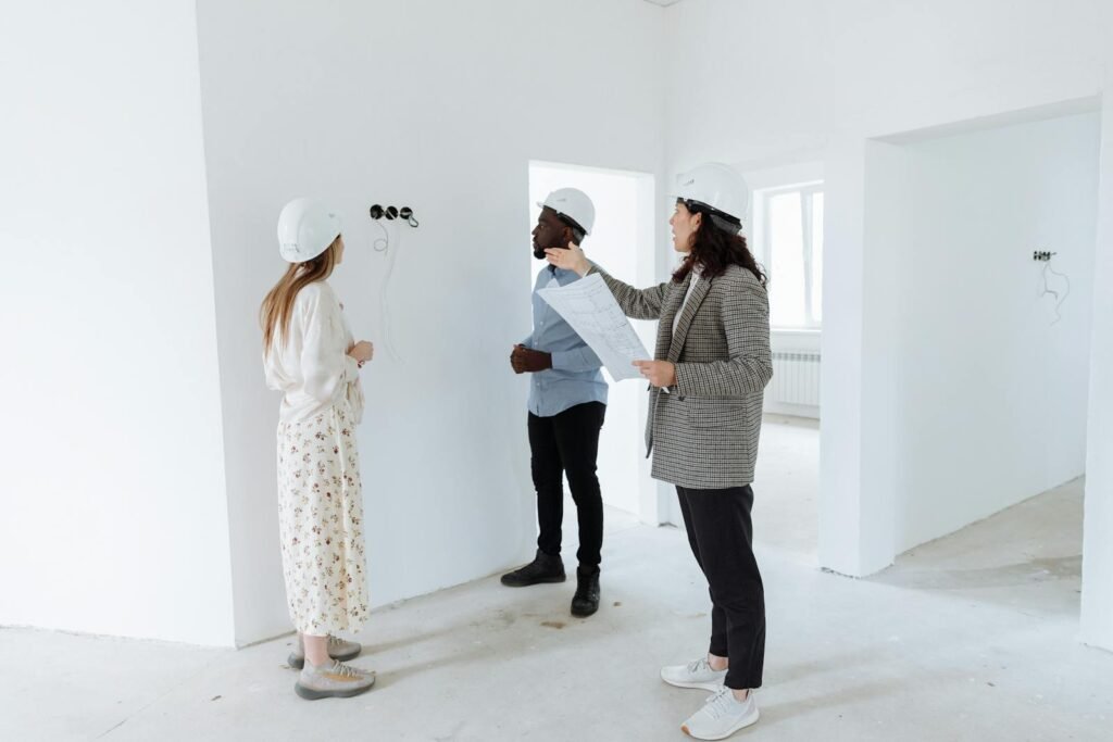 Contacto Cristian Flore Aranjuez Three professionals discuss design plans inside a new house wearing hard hats.